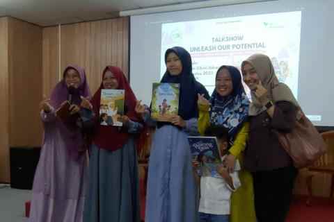 A group of Indonesian women hold up illustrated children's books