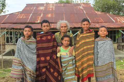 5 children stand in a line, each wrapped in a cloth of intricate design. An elderly woman also stands in the middle.