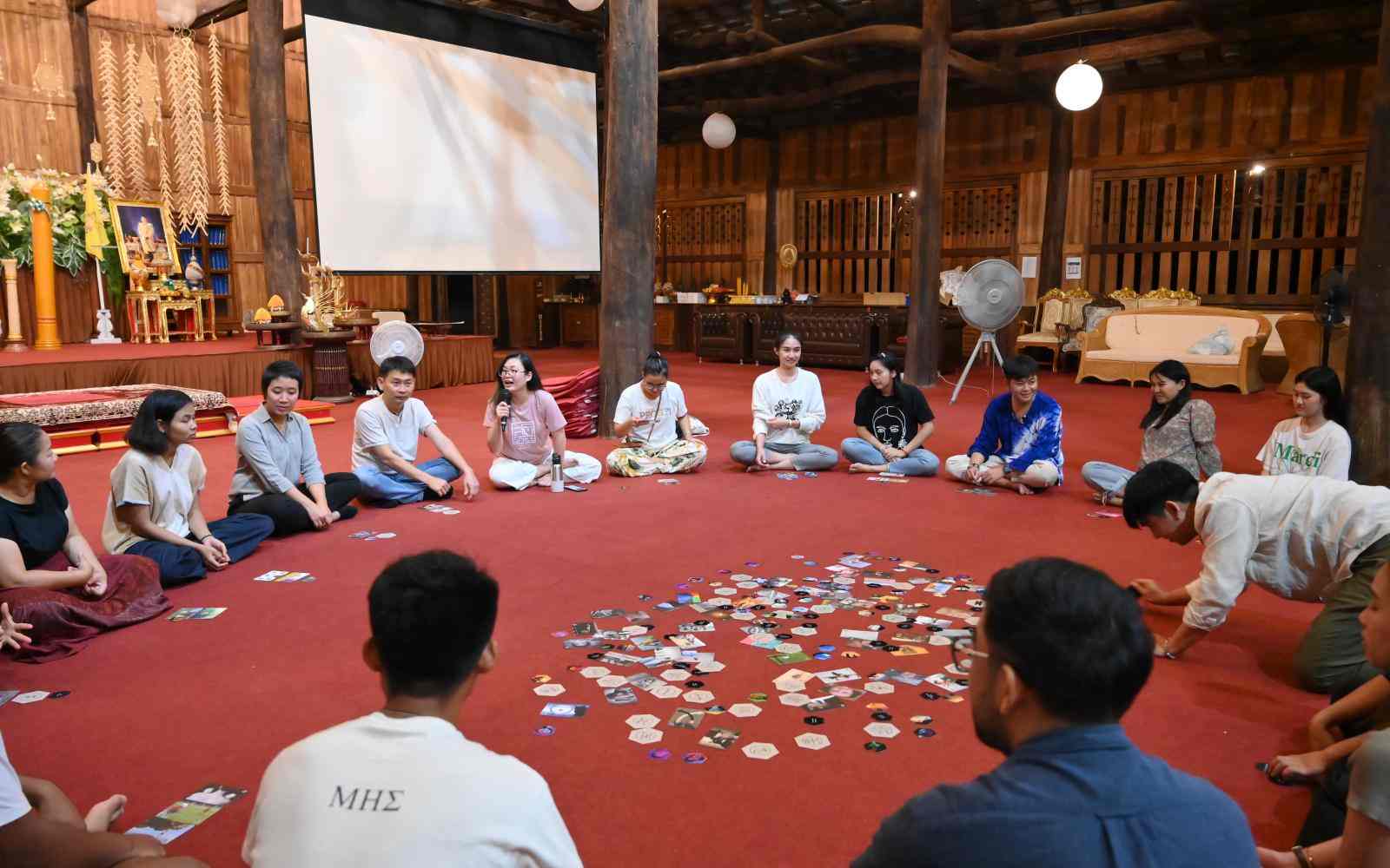 A circle of people sitting on a carpeted floor with tokens in the middle
