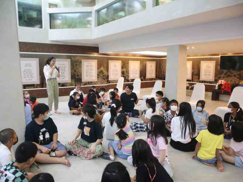 Thai children sitting on the floor, listening to a woman
