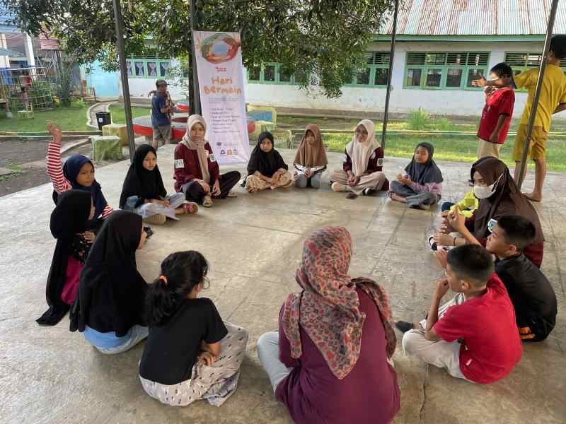 A circle of Indonesian women and children sitting on the ground